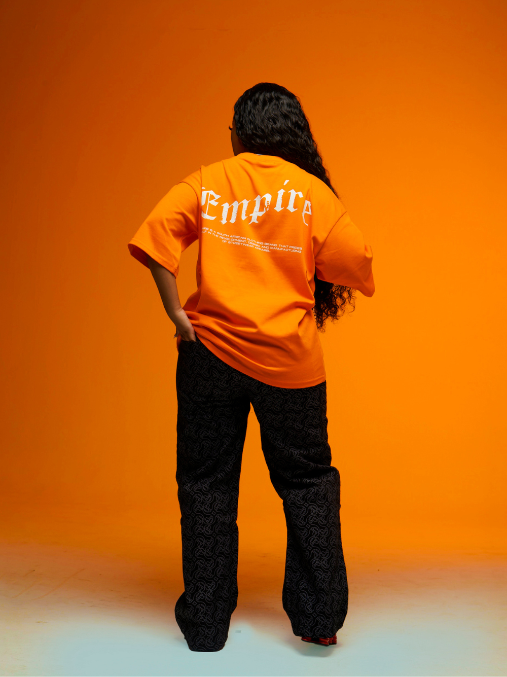 Empire orange oversized graphic t shirt at unseen grail. local brands south africa. streetwear. men and women. studio image female model full outfit back view