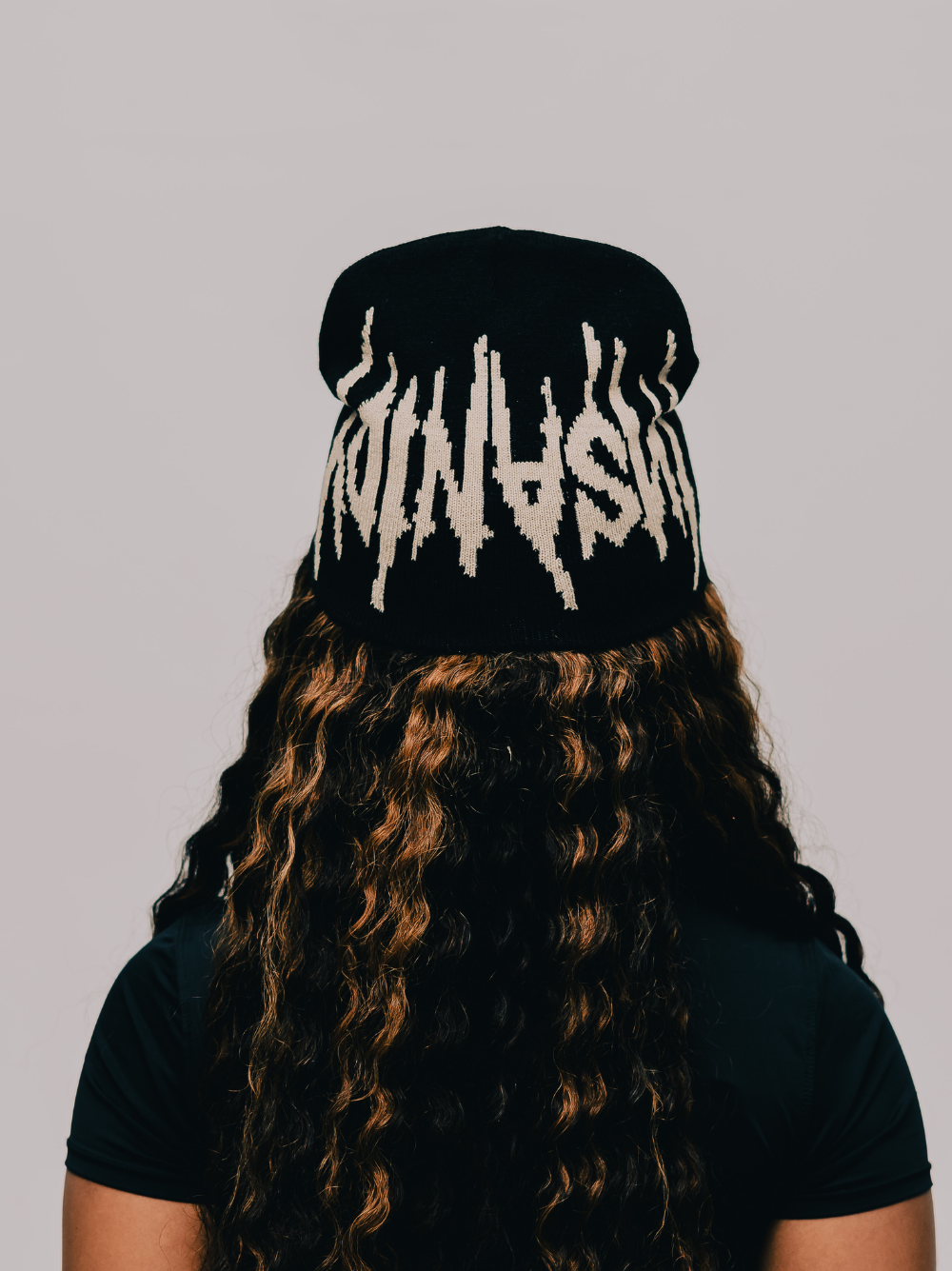 Insanidy knitwear black beanie at unseen grail. local brands south africa. streetwear. men and women. studio image female model behind